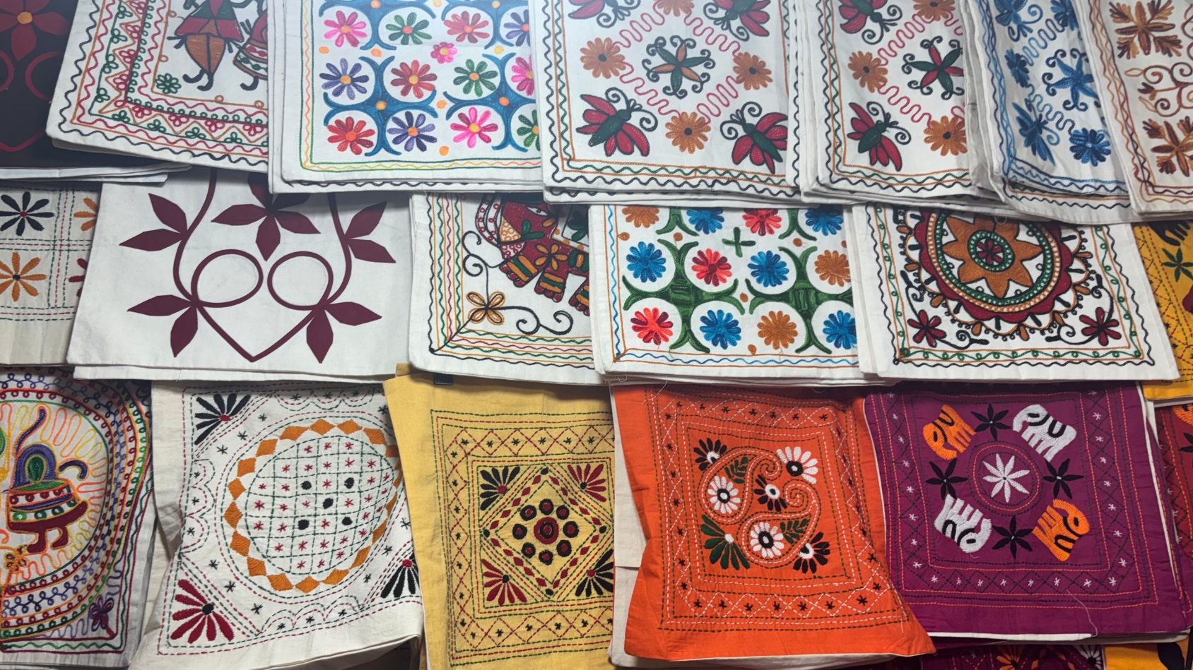 <p>Bright, embroidered cushions and fabrics showcasing traditional floral and geometric patterns.</p>