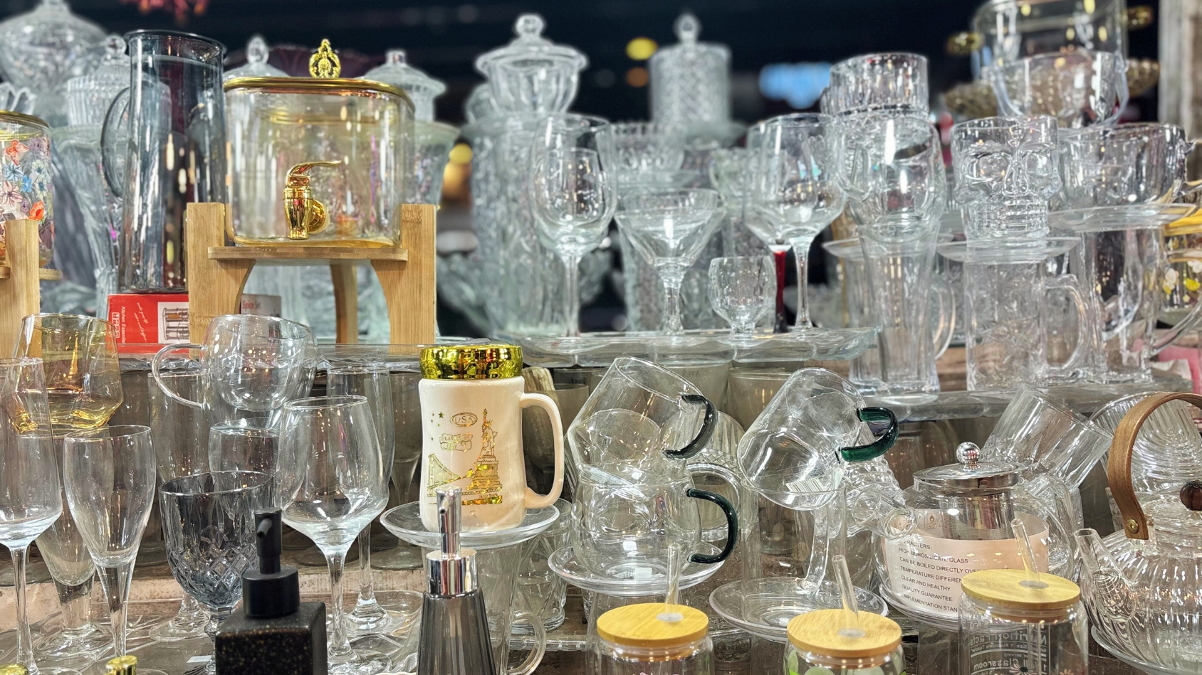 <p>Glassware such as wine glasses, mugs and jars glints under shop lights.</p>